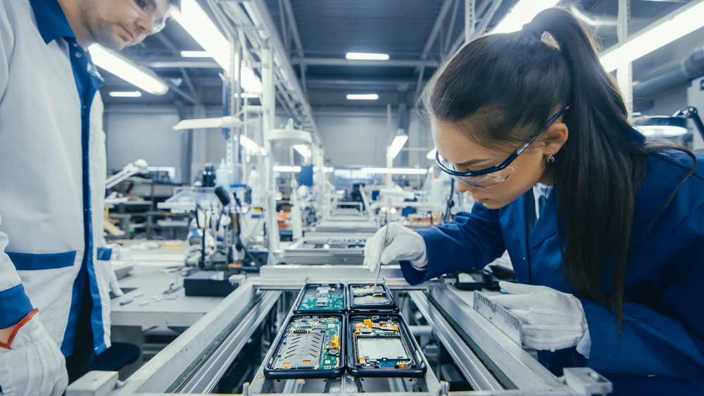Electronics factory workers assembling circuit boards by hand on assembly line. 