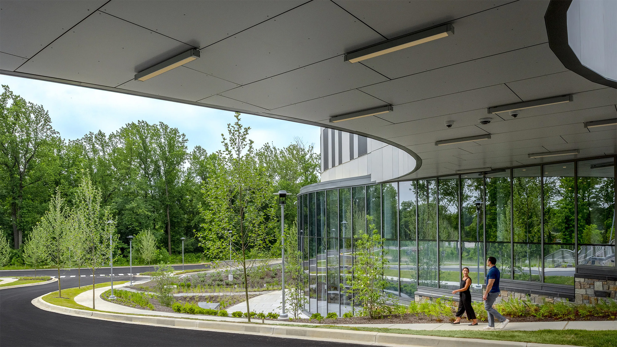 People walking outside of glass building surrounded by foliage
