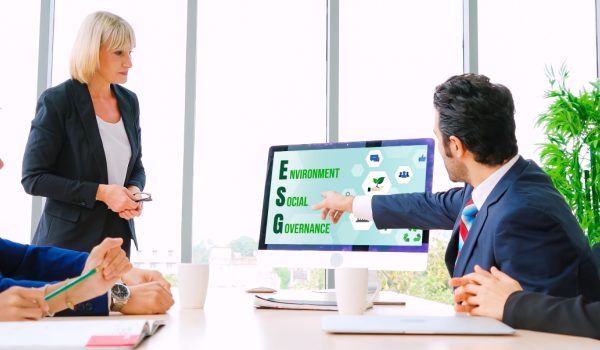 a group of people gathered around a meeting room table looking at a screen with the meaning of ESG portrayed on it